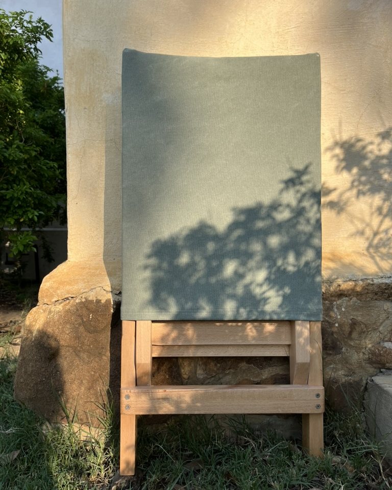 Beech folding chair with olive canvas against a wall